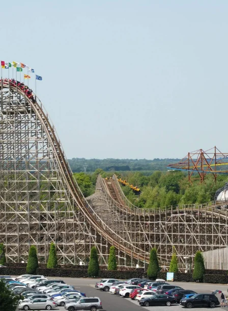 Family enjoying a sunny day at a theme park near The Gateway Hotel, wooden rollercoaster and car park visible