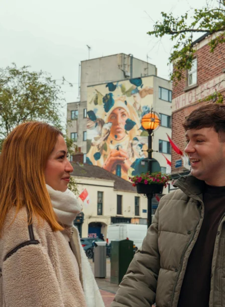 A smiling couple enjoys a walk near The Gateway Hotel Dundalk, surrounded by vibrant street art and historic buildings.