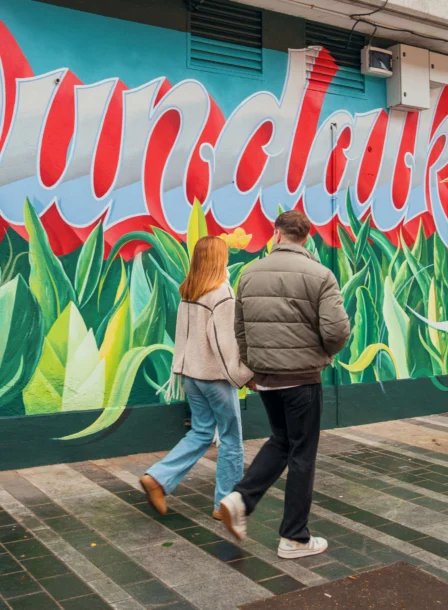 A couple strolling past colourful "Dundalk" mural near The Gateway Hotel.
