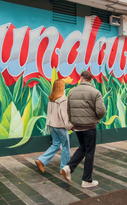 A couple strolling past colourful "Dundalk" mural near The Gateway Hotel.
