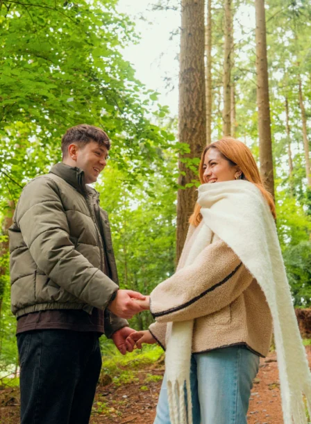 A couple holds hands, smiling in a lush green forest near The Gateway Hotel Dundalk.