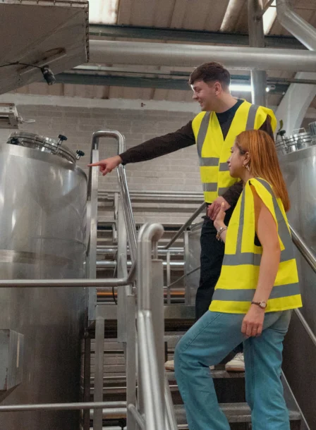 A couple wearing yellow vests explore large brewing tanks at The Gateway Hotel Dundalk.