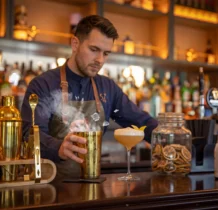 A bartender mixes cocktails at a warm, inviting hotel bar.