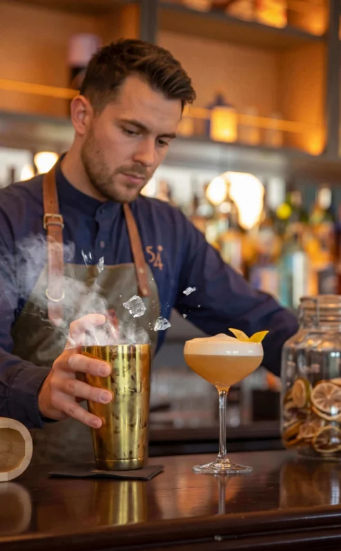 A bartender mixes cocktails at a warm, inviting hotel bar.