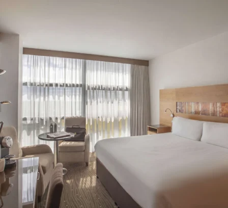 Modern hotel room with a large bed, seating area, and warm lighting.