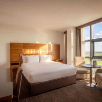 Bright hotel room with a cosy bed, seating area, and scenic countryside view.