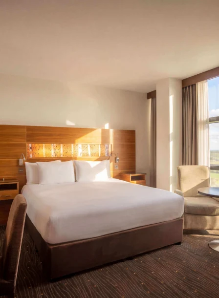 Bright hotel room with a cosy bed, seating area, and scenic countryside view.