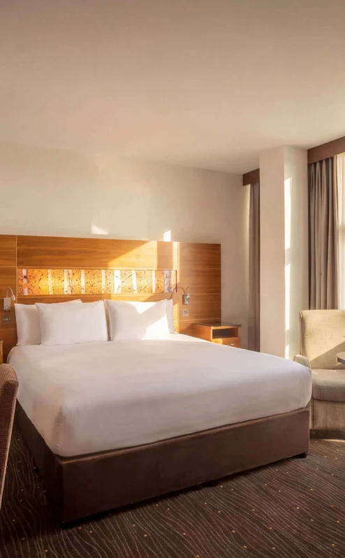 Bright hotel room with a cosy bed, seating area, and scenic countryside view.