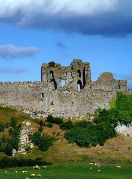 Family exploring historic ruins atop a lush green hill under a vibrant blue sky.