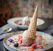 Elegant dessert presentation with ice cream, berries, and decorative cone on a restaurant table.
