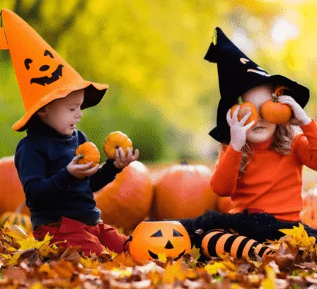 Family children in Halloween hats playing with small pumpkins among autumn leaves at The Gateway Hotel grounds