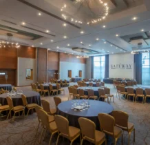 Spacious hotel event hall with round tables set for a gathering, warm lighting, and large windows.