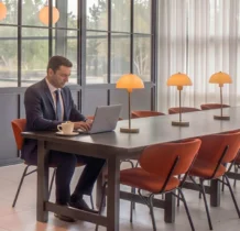 Businessman working on laptop in sunlit hotel lounge with modern décor.