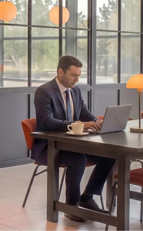 Businessman working on laptop in sunlit hotel lounge with modern décor.