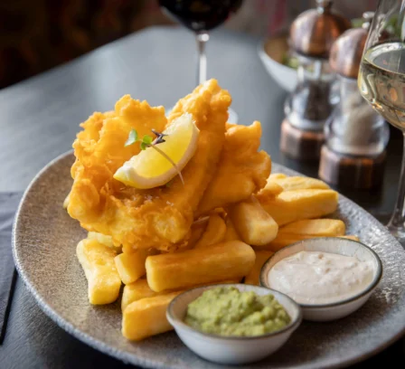 A delicious plate of fish and chips with mushy peas and tartar sauce, set on a restaurant table.