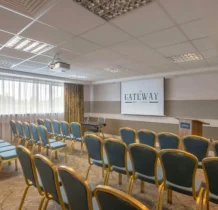 Elegant hotel conference room with rows of chairs and large window. Projector screen displays "The Gateway Hotel".