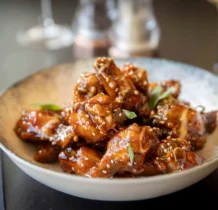 A bowl of glazed chicken wings with sesame seeds at The Gateway Hotel's restaurant.