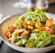 Fresh salad with vibrant greens and sliced tomatoes served on a rustic table.