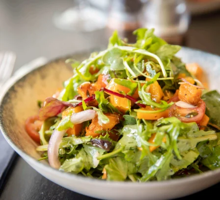 Fresh salad with vibrant greens and sliced tomatoes served on a rustic table.