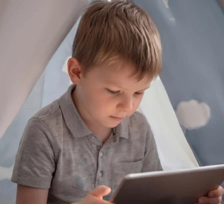 Child in a cosy tent, focused on a tablet with playful hot air balloon decor.