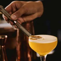 A hand garnishes a cocktail with a dried orange slice, set in a cosy bar at The Gateway Hotel.