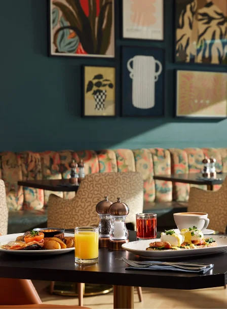 A cosy cafe-style dining area with breakfast dishes and juice on a sunlit table.