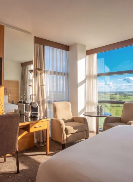 Modern hotel room with scenic countryside view, cosy seating, and inviting natural light.