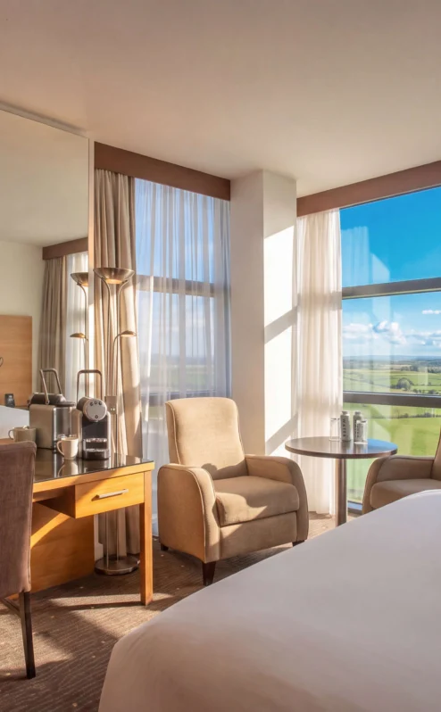 Modern hotel room with scenic countryside view, cosy seating, and inviting natural light.