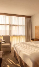 Spacious, sunlit hotel room with large bed, seating area, and elegant decor at The Gateway Hotel.