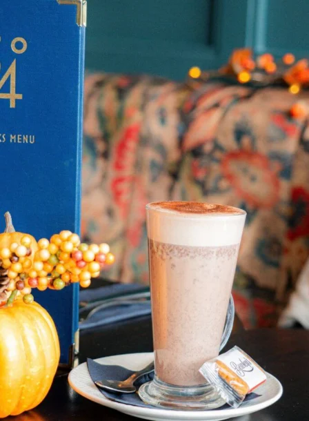 Cosy hotel café table with latte, autumn pumpkins, 54 drinks menu and seasonal decor
