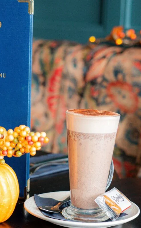 Cosy hotel café table with latte, autumn pumpkins, 54 drinks menu and seasonal decor